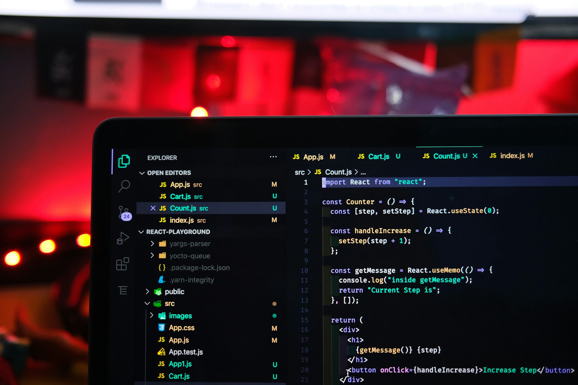 Close de uma tela de laptop exibindo um editor de código (VS Code) com scripts em JavaScript e React, representando o uso de modernas Linguagens de Programação no desenvolvimento de software. O ambiente possui iluminação suave ao fundo com tons de vermelho.