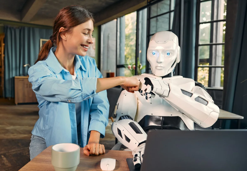 Uma mulher sorridente em uma camisa azul faz um "soquinho" (fist bump) com um robô humanoide branco que está sentado em frente a um laptop. A imagem representa uma parceria amigável e bem-sucedida entre humanos e IA/robôs, possivelmente resultando de prompts colaborativos.