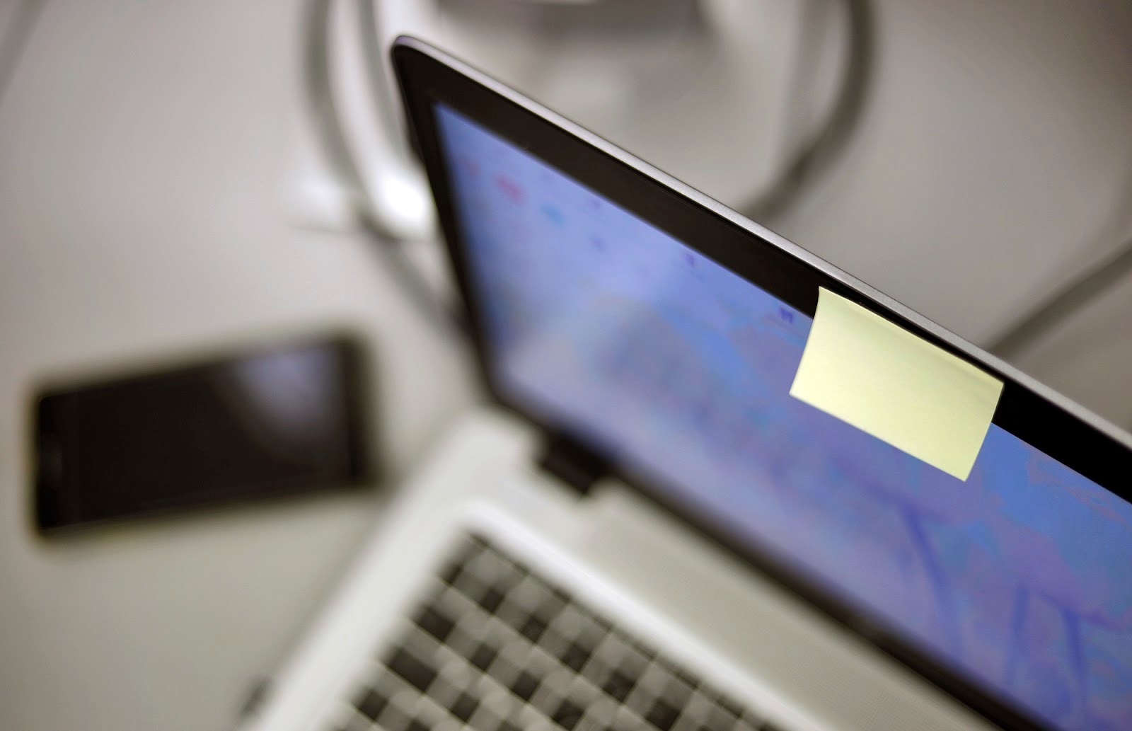 Um close-up lateral de um notebook com um post-it amarelo cobrindo a lente da webcam. Uma solução caseira e eficaz para tapar sua webcam.