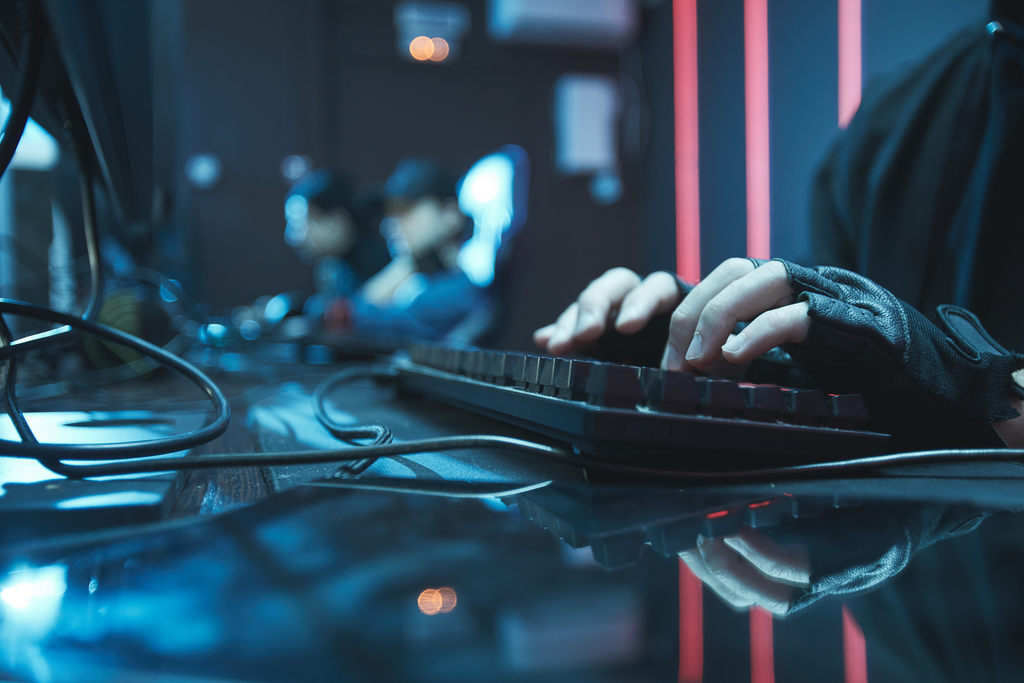 Visão em close-up das mãos de um profissional, possivelmente de um Red Team, digitando rapidamente em um teclado gamer iluminado com luzes vermelhas. Foca na ação prática de cibersegurança e como ganhar dinheiro hackeando em testes de invasão.