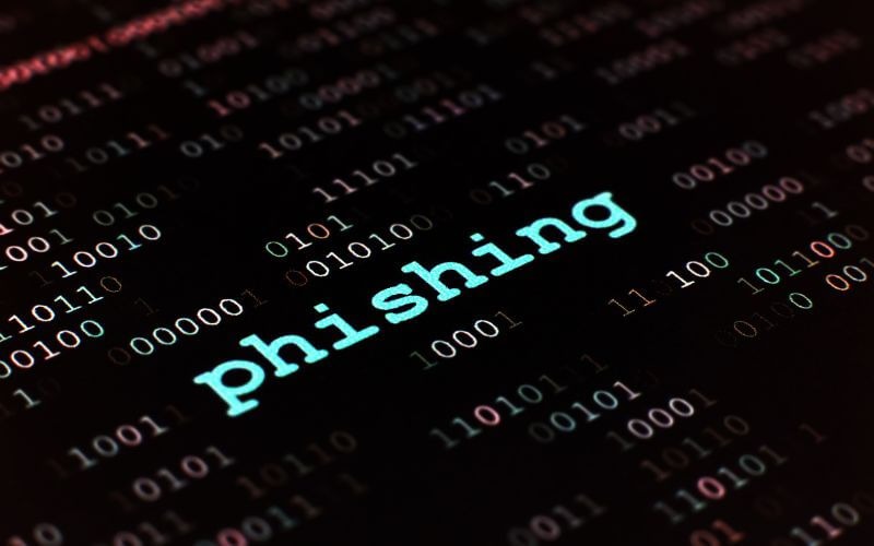 A palavra "phishing" escrita em letras verdes neon em destaque sobre um fundo de códigos binários e digitais escuros, focando no conceito técnico do ataque de phishing.